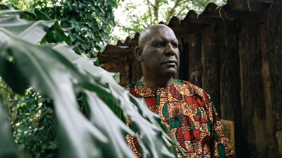 Homem negro em camisa africana, natureza e estrutura rústica