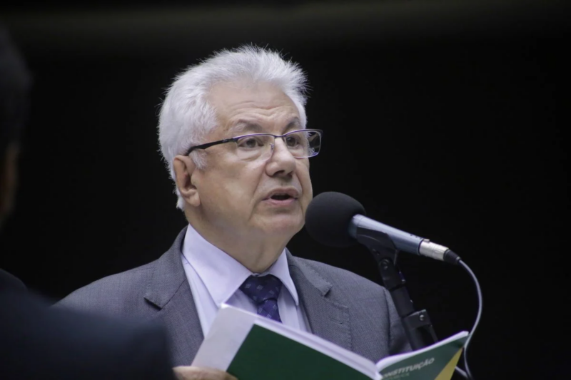 Homem discursa, segurando a Constituição, em evento formal