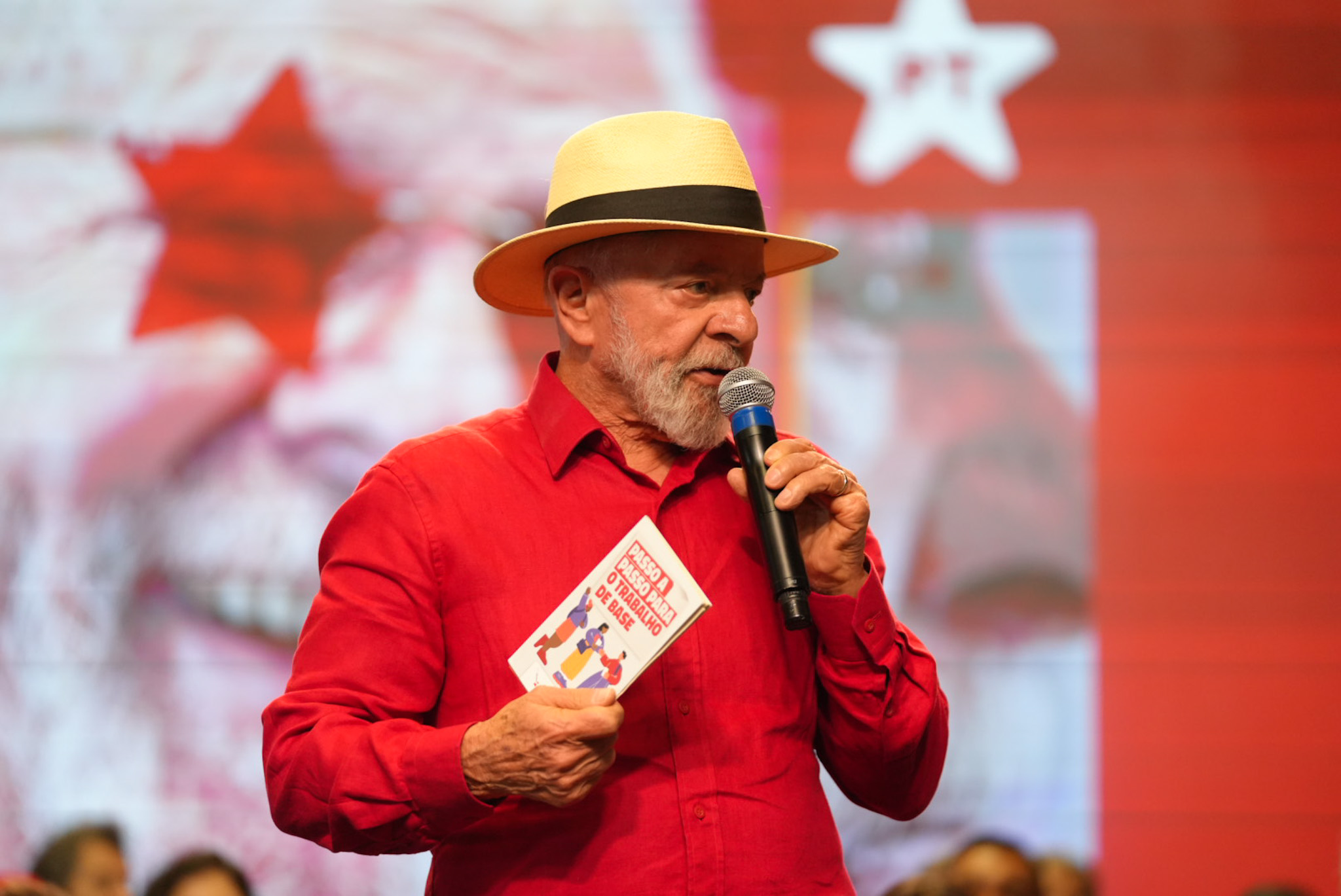 Lula discursa, segurando material de trabalho de base do PT.