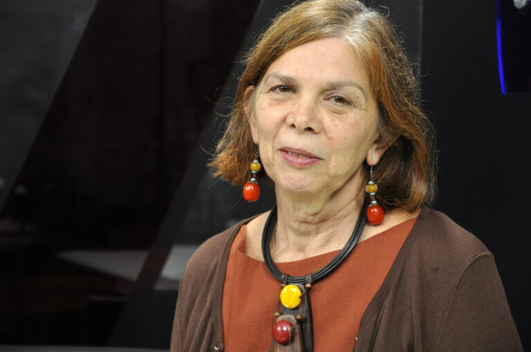 Mulher madura, expressão calma e joias artesanais vibrantes.