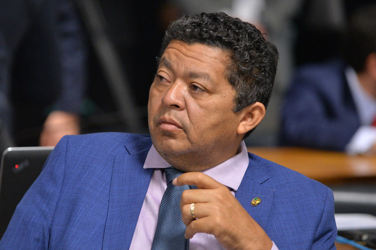 Homem em terno azul, expressão séria, ambiente formal.