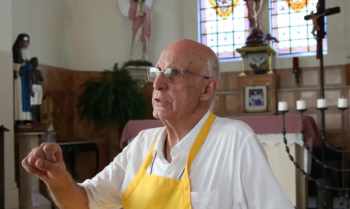 Homem idoso discursa com paixão em ambiente religioso.