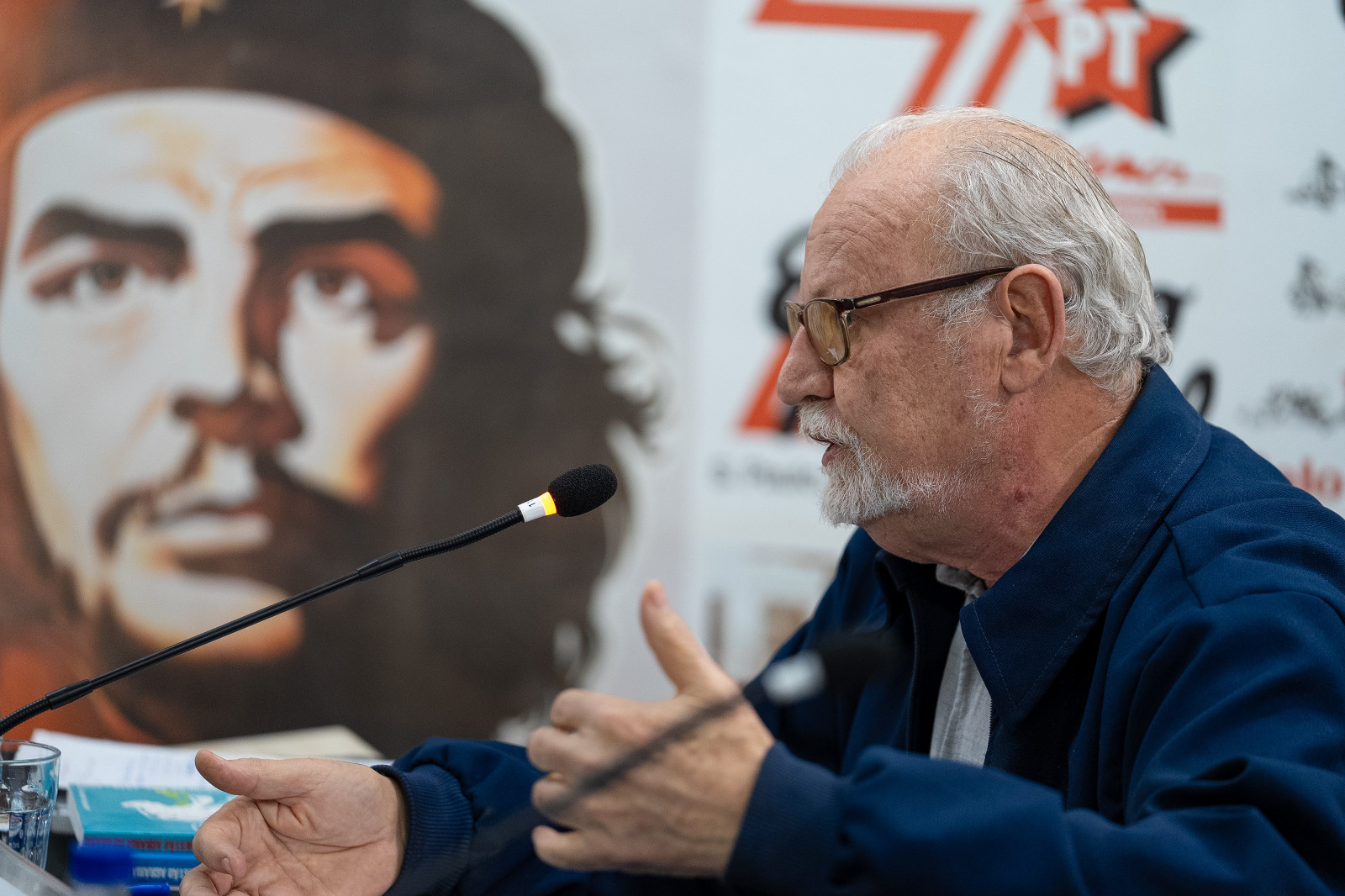 Homem discursa com Che Guevara e logo do PT ao fundo