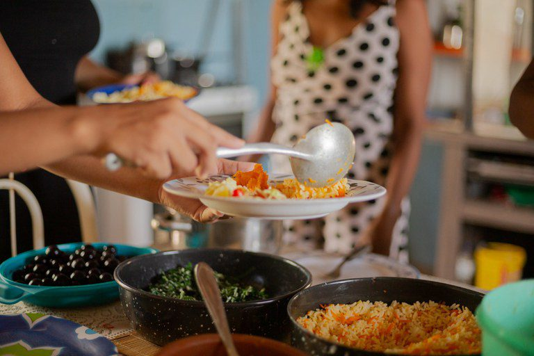Mãos servindo refeição caseira em ambiente de partilha e comunidade