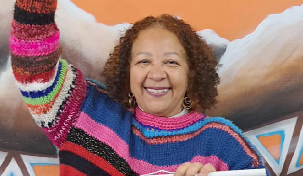 Mulher sorridente em suéter colorido levanta o braço.