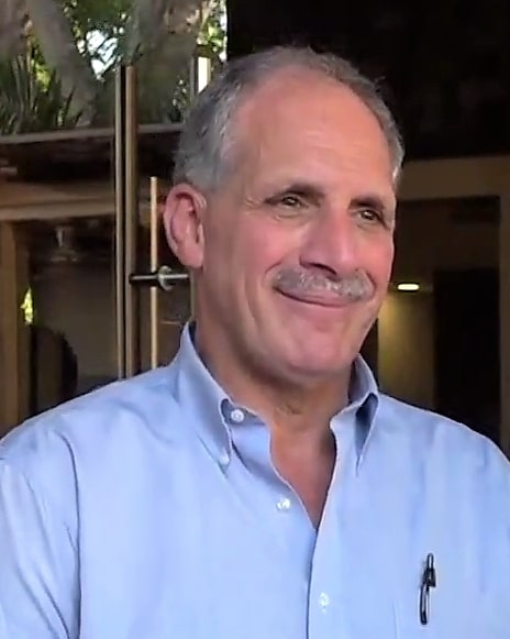 Homem sorridente de camisa azul e bigode.