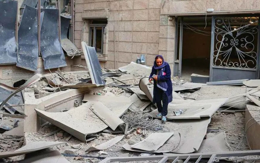 Mulher caminha entre escombros após destruição urbana